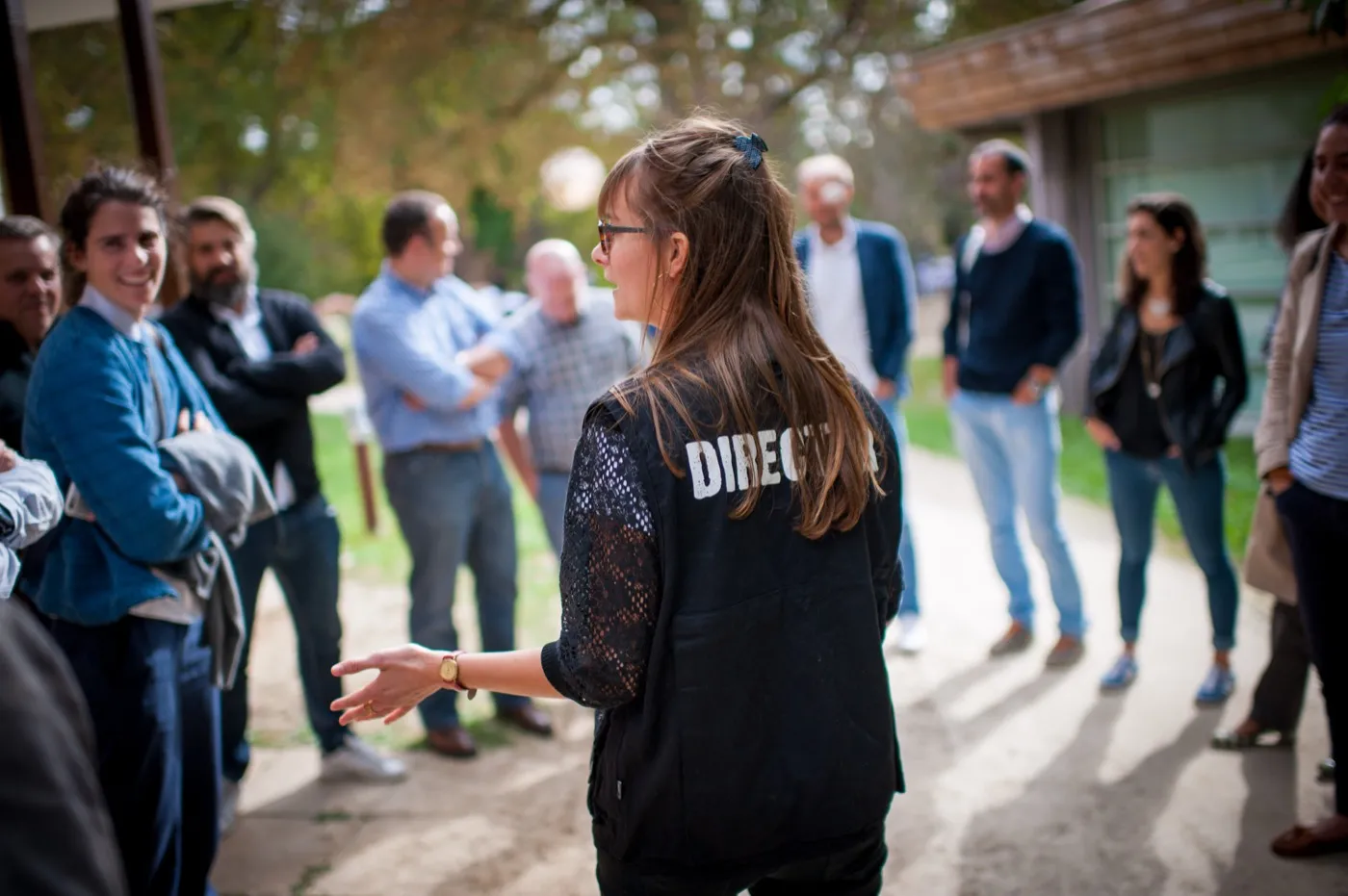 Une directrice, veste floquée DIRECTOR, de dos, briefe son équipe en cercle avant le tournage Roïka